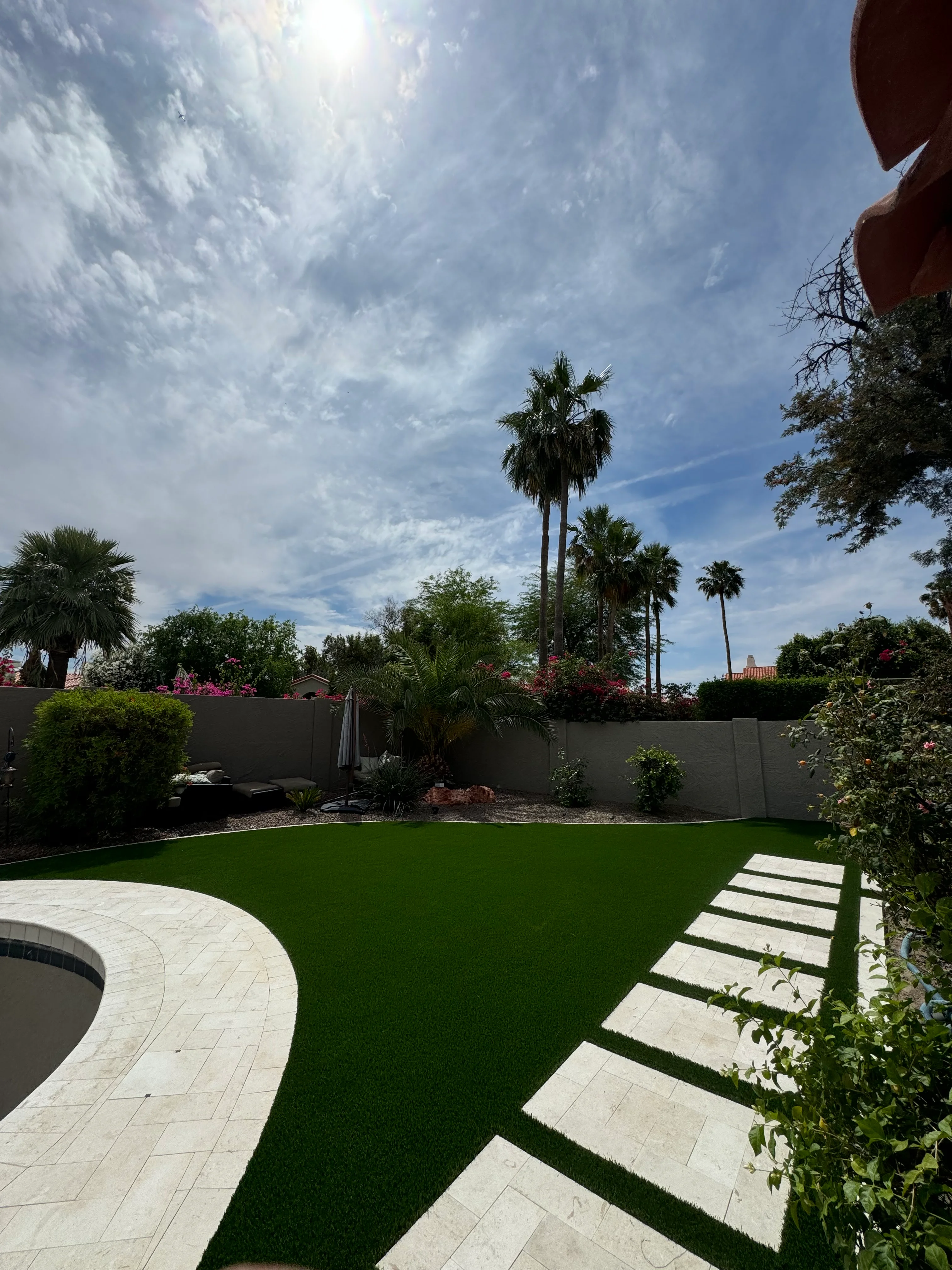 Modern backyard with synthetic grass, stone pavers, palm trees, and flowering plants