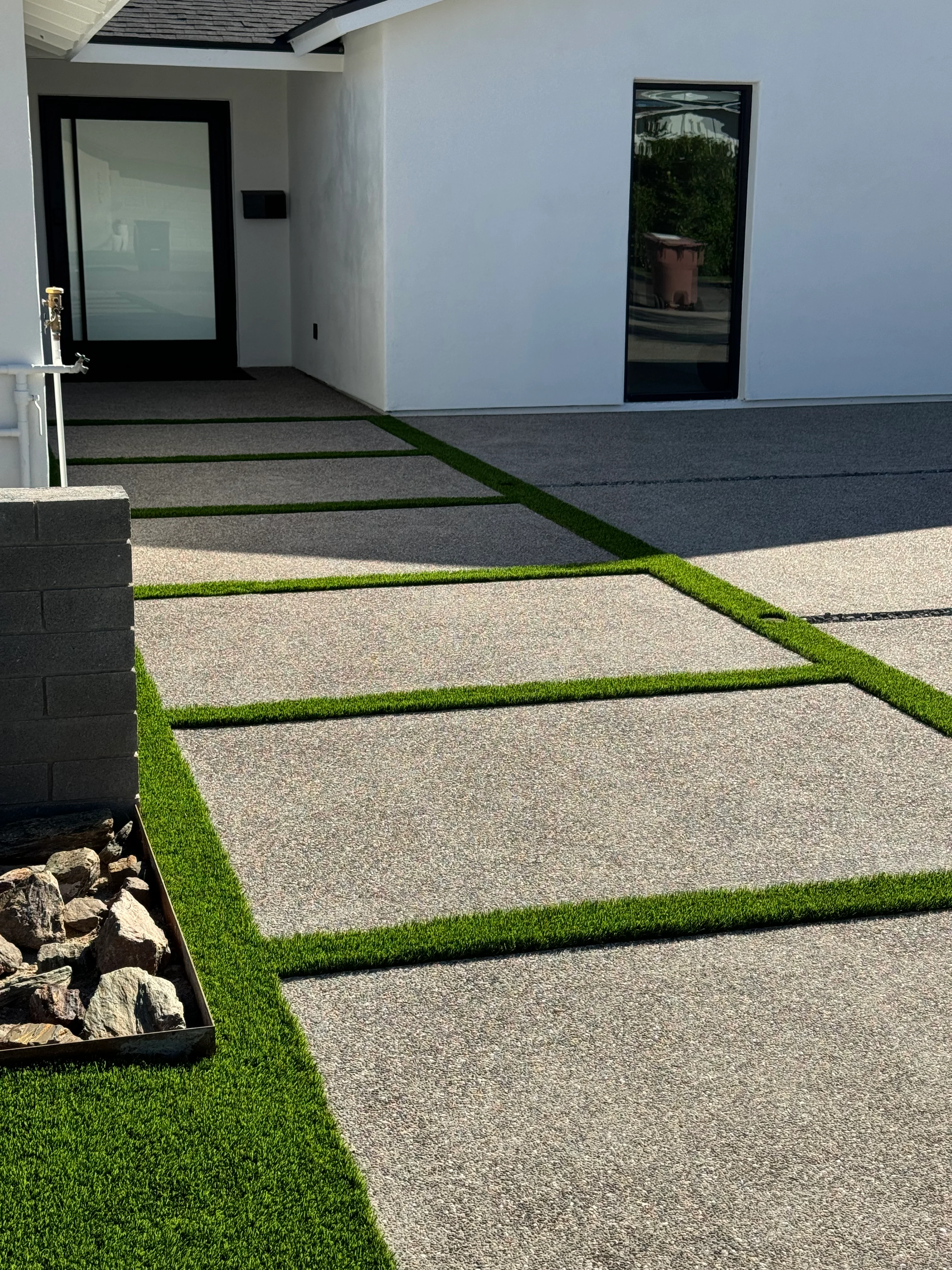 Modern hardscape with concrete pavers and synthetic turf borders leading to contemporary home entrance