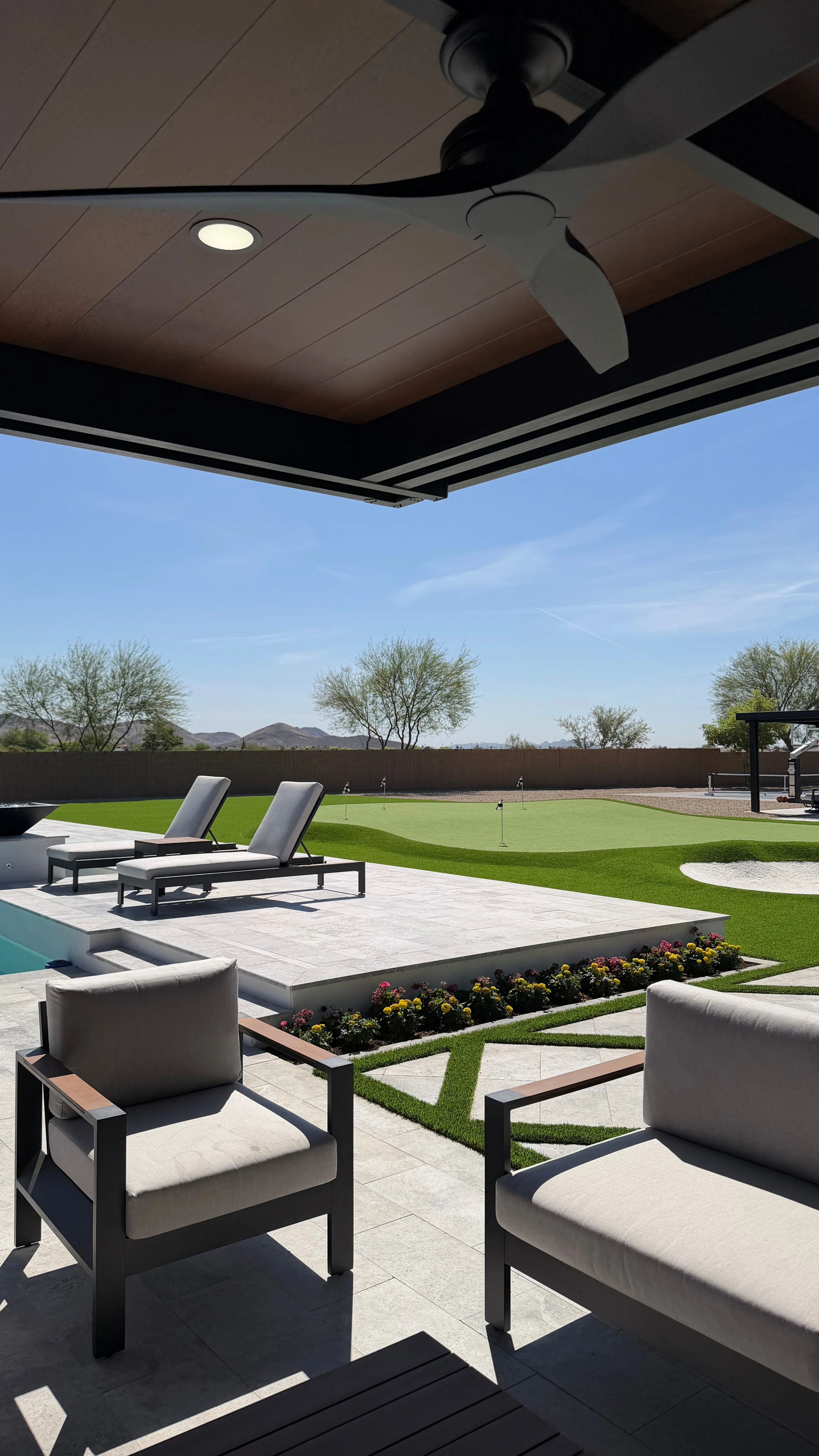 Modern patio with lounge chairs, shade structure, lawn, and desert mountain views