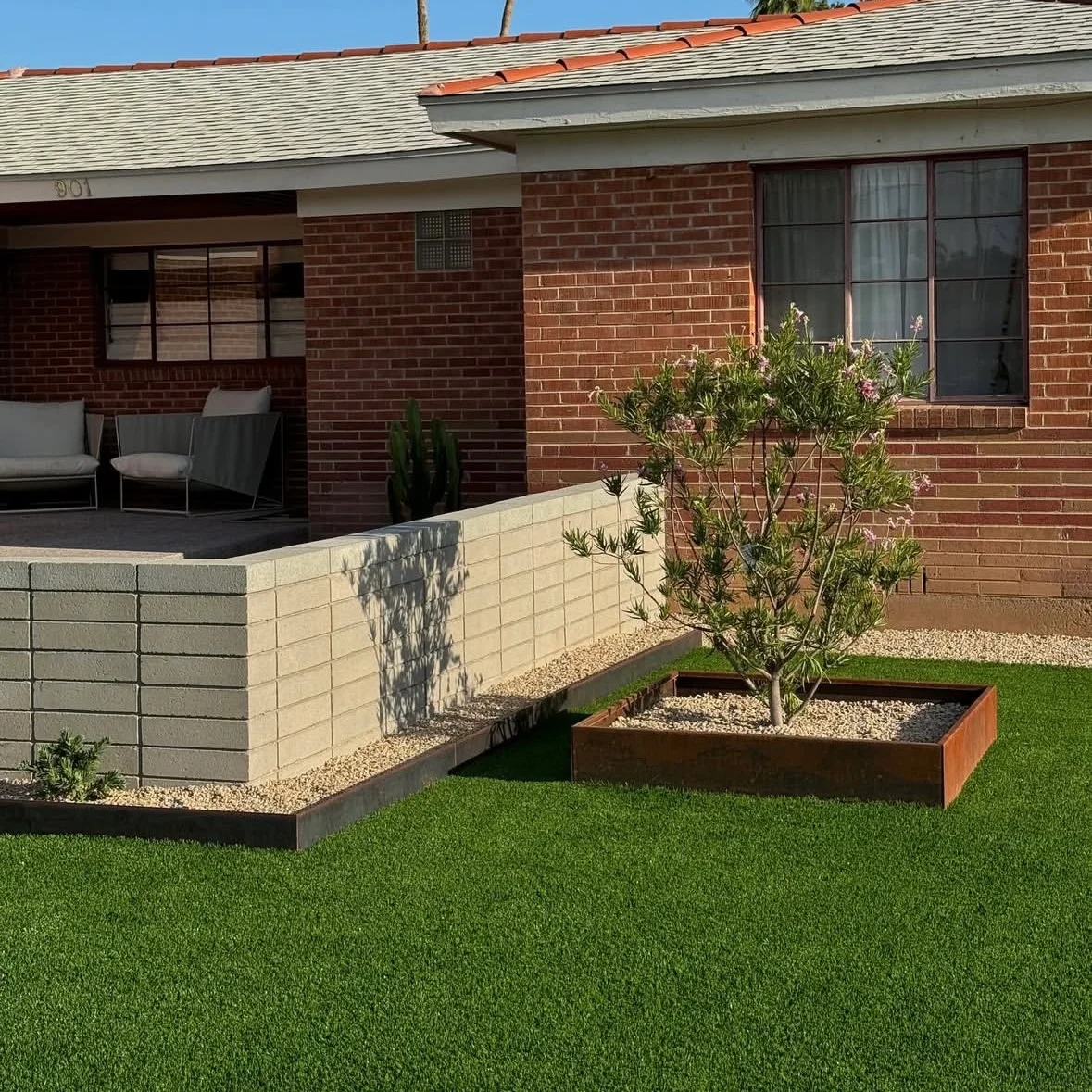 Modern backyard with synthetic turf, concrete retaining wall, and planted landscape beds