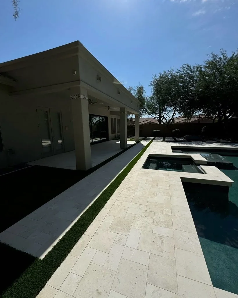 Modern poolside patio with travertine pavers, pergola, and synthetic turf landscaping