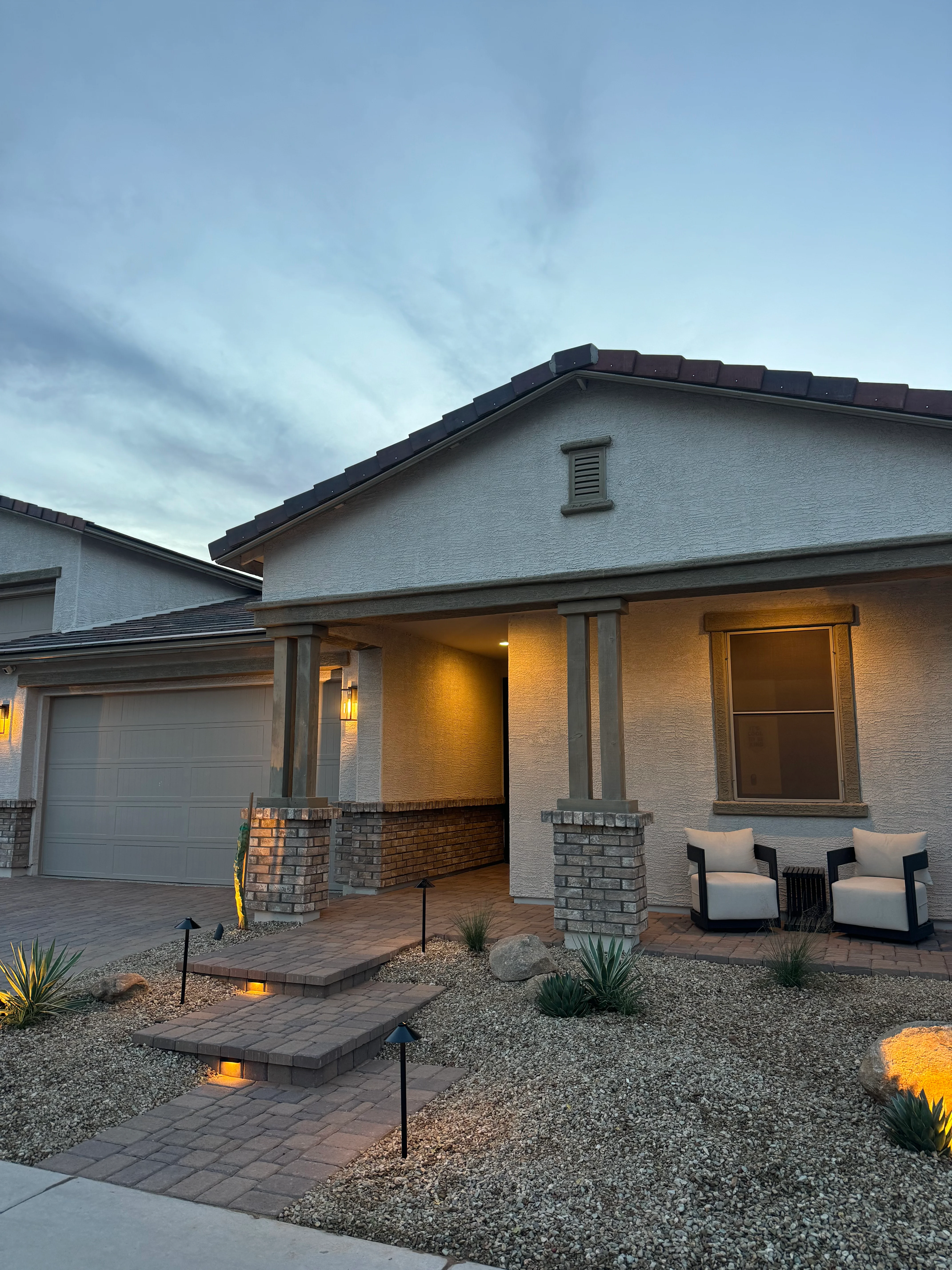 Modern home with lit paver pathways, gravel landscaping, and desert plants at dusk