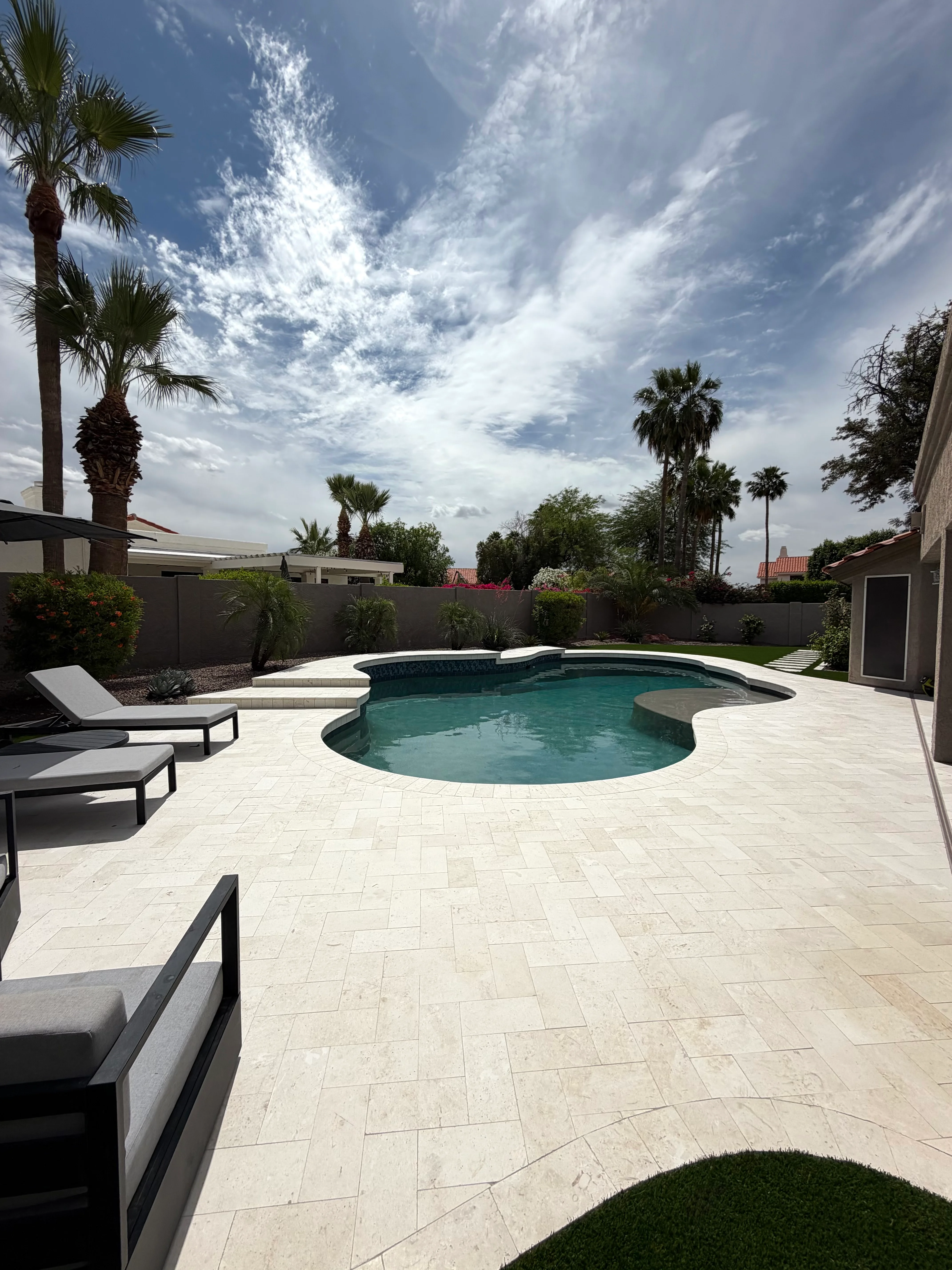 Curved pool deck with light pavers, lounge chairs, and palm trees in Phoenix backyard