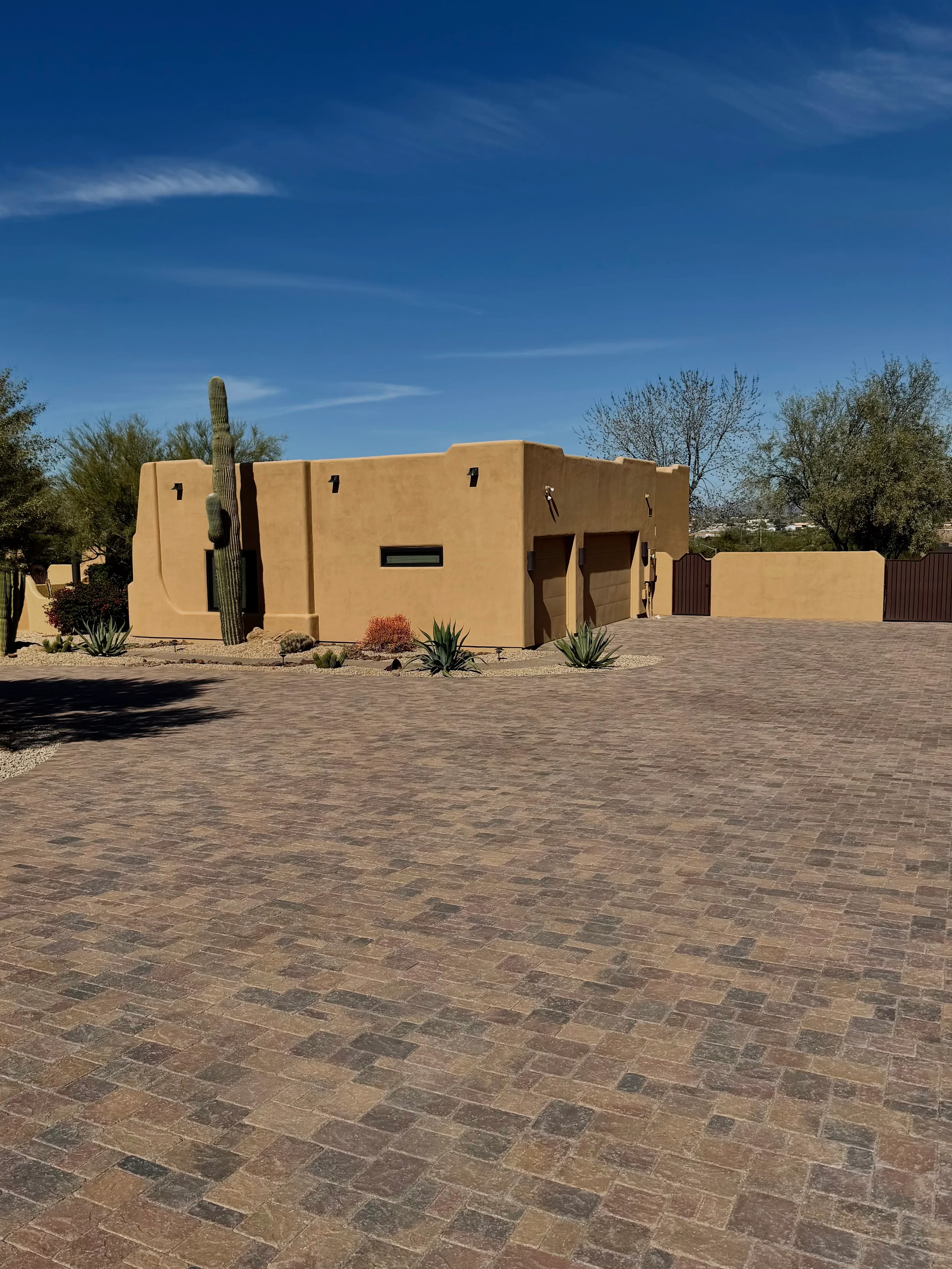 Tan and brown geometric paver driveway in front of modern stucco home with desert landscaping
